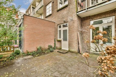 a back yard with plants and flowers in the fore - windowed apartment building, which has been closed for several years
