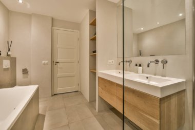Modern bir banyo, iki lavabo ve duvarında büyük bir ayna olan lavabonun yanında beyaz bir küvet var.
