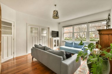 Odanın ortasında ahşap döşeme ve mavi bir kanepe olan oturma odası büyük bir pencere.