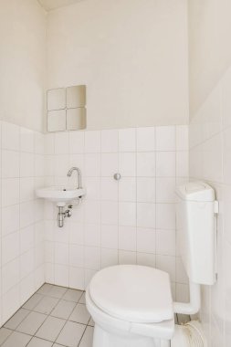 Beyaz fayanslı küçük bir banyo ve köşede bir tuvalet, üzerinde bir ayna var.