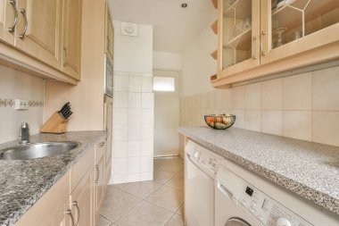 Granit tezgahlı çok temiz bir mutfak ve odanın ortasındaki beyaz çamaşır makinesi boş.