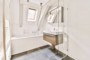 Lavabosu, aynası ve küveti olan bir banyo pencerenin yanında açık bir tavan penceresi var.