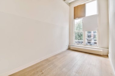 Beyaz duvarları ve sağ tarafında ahşap döşemeleri olan boş bir oda. Sokağa bakan bir pencere var.