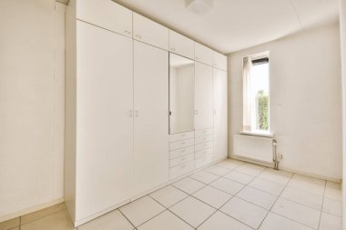 Beyaz dolapları ve zeminde fayansları olan boş bir oda. Duvarda bir pencere var.