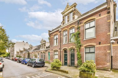 the street in front of an old brick building, with cars parked on the side and trees lining the road