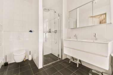 Beyaz duvarları ve yerde siyah fayansları olan modern bir banyo. Lavabonun yanında bir tuvalet var.