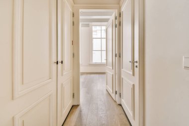 Beyaz duvarları ve yan yana ahşap döşemeleri olan uzun bir koridor diğer odalara açılıyor.