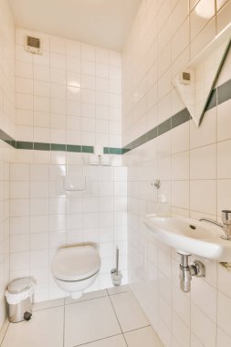 Duvarlarında beyaz fayanslar ve yeşil süslemeler olan küçük bir banyo ve lavabonun yanında bir tuvalet.