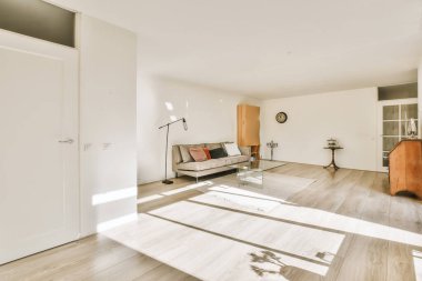 Ahşap döşemeleri ve beyaz duvarları olan bir oturma odası, sağ taraftaki duvarda büyük bir ayna var.