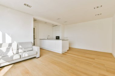 Ahşap döşemeleri ve beyaz duvarları olan bir oturma odası. Bölgede büyük bir mutfak adası da var.