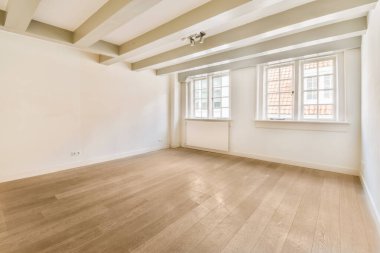 Odanın ortasında beyaz duvarları ve ahşap döşemeleri olan boş bir oda, dışarı bakan bir pencere var.