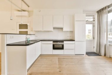 a kitchen area with white cabinets and black counter tops on the island in front of the window is an outside view