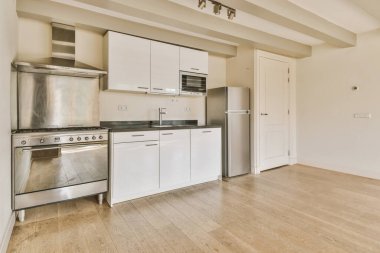 Tezgahın üstünde beyaz dolaplar ve paslanmaz eşyalar olan boş bir odada ahşap döşeme olan bir mutfak.