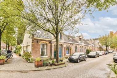 a street with cars parked on the side and trees lining the road in front of the house, surrounded by green leaves