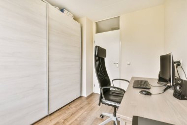 an office space with wood flooring and white walls, including a computer on a desk in front of the wall