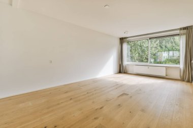 an empty living room with wood flooring and large window looking out onto the trees in the garden behind it