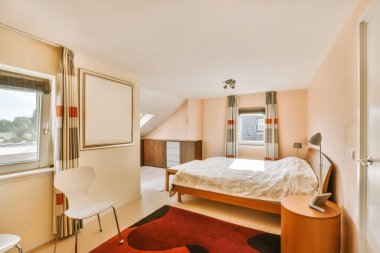 Yatağı, masası ve sandalyesi olan bir yatak odası. Sokağa bakan açık bir pencerenin yanında.