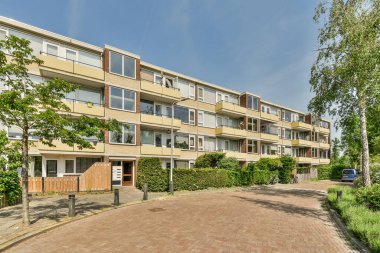 Banliyöde bir apartman kompleksi, sokağın her iki tarafında ağaçlar ve çalılar var.