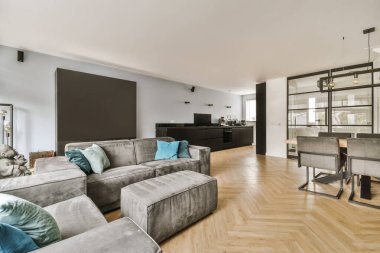 Odanın ortasında ahşap döşemeli ve gri koltuklu bir oturma odası yemek masası.