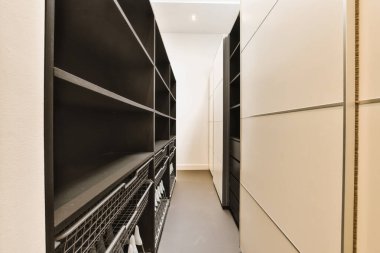 Her iki tarafında siyah beyaz dolaplar olan uzun, dar bir koridor, bizi başka bir odaya götürecek açık bir kapıya götürüyor.