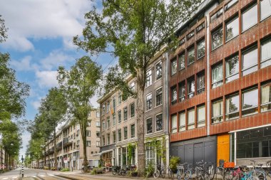 Kaldırımlarda bisikletleri ve arka planda binaları olan bir şehir caddesi var. Bulutlu mavi bir gökyüzü var.