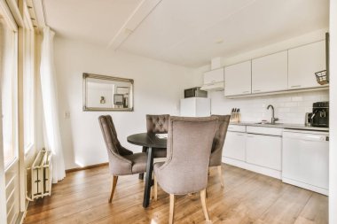 a kitchen and dining area in a room with white cabinets, wood flooring and an oven on the wall