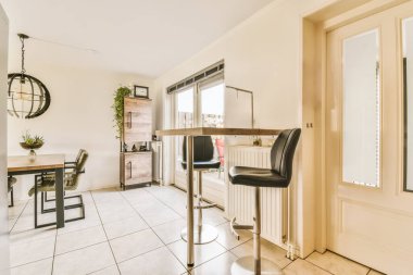 Beyaz fayans döşemeli, bej duvarlı ve dış kapıya açık bir evde mutfak ve yemek odası.