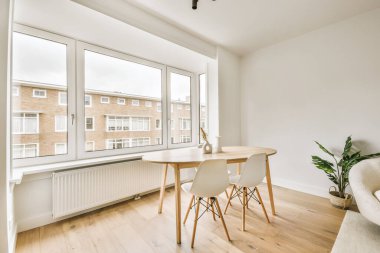 Oturma odasında bir yemek masası ve sandalyeler. Büyük pencereleri olan şehir manzaralı bir yer.