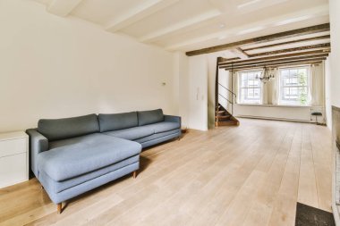 Odanın ortasında beyaz duvarları ve ahşap döşemeleri olan bir oturma odası mavi bir kanepe, açık bir şömine.