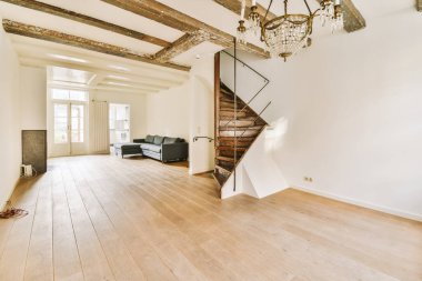 Ahşap zeminli ve tavanında kirişler olan boş bir oturma odası var. İkinci kata çıkan bir merdiven var.