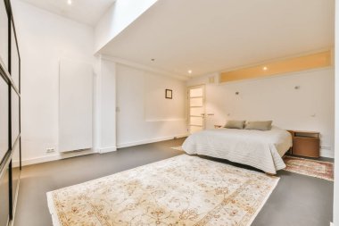 Yatak odası. Yerde halı var. Yatağın önünde ve arkasında banyo kapısı.