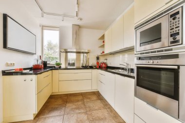 Bu fotoğraftaki tezgahların üzerinde beyaz dolaplar ve siyah tezgahlar olan modern bir mutfak içeriden çekilmiştir.