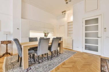 Odasında ahşap döşeme ve beyaz duvarlar olan bir yemek odası siyah ve beyaz halılarla süslenmiş.