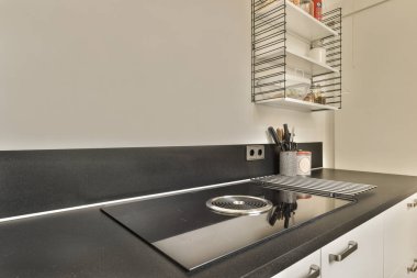 a kitchen with black counter tops and white cabinets in the corners on the left is an open shelf above the sink