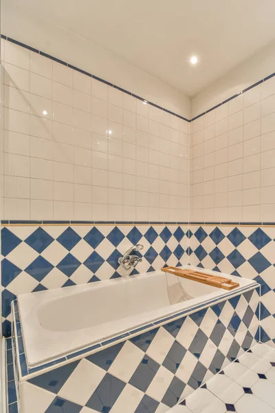 a tiled bathroom with blue and white tiles on the walls, along with a large bathtub in the corner