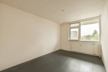 Beyaz duvarları ve yerde siyah kiremitleri olan boş bir oda. Köşede büyük bir pencere var.