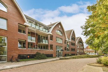 an apartment complex in the netherlands with red brick walls and green trees on either side, there is a blue sky