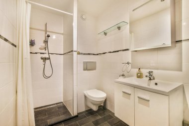 a white bathroom with black tile flooring and gray tiles on the walls, along with a toilet in the corner