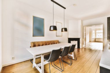 a dining room with white walls and hardwood flooring, including a wooden table surrounded by four black leather chairs
