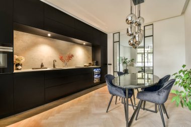 a kitchen and dining area in a modern home with black cabinets, marble countertops, white walls and wood flooring