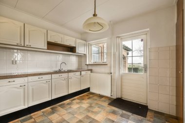 a kitchen area with tile flooring and white cupboards on either side of the room, there is an open door that leads