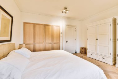 a bedroom with white bedding and wooden cabinets on the wall behind it is a large mirror hanging above the bed