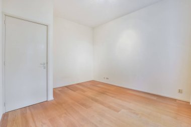 Ahşap zemini ve beyaz duvarları olan boş bir oda. Odanın sol tarafına açılan bir kapı var.