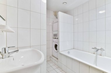 a bathroom with white tiles and a toilet in the corner, next to a bathtub that is on the wall
