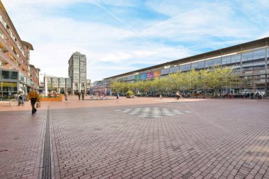 a city square with people walking and sitting on benches in the middle part of the street, surrounded by tall buildings