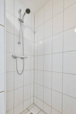 Duvarında beyaz fayanslar olan bir banyo ve küvetin önündeki duvara monte edilmiş duş başlığı.