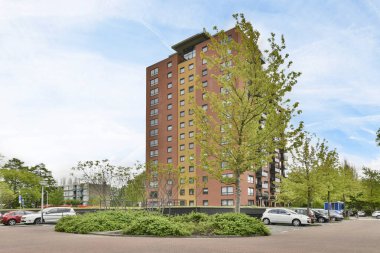 Amsterdam, Netherlands - 10 April, 2021: an apartment complex with cars parked in the parking lot and trees growing on the side of the building, as seen from the street