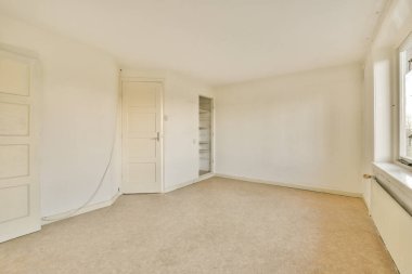 an empty living room with white walls and beige carpet, there is a window in the wall to the right