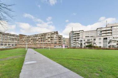 Amsterdam, Netherlands - 10 April, 2021: a grassy area in front of an apartment building on a sunny day with blue sky and fluffy white clouds above