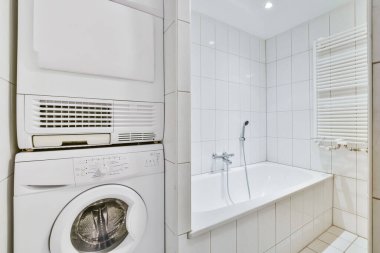 a laundry room with a washer and dryer in the corner, next to a bathtub on the wall